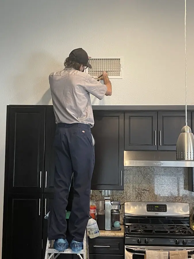 Technician inspecting an air vent during HVAC service in Lansing
